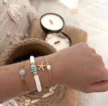 Load image into Gallery viewer, Was gibt es Schöneres auf gebräunter Sommerhaut? Ein wunderschönes Muschelarmband - handgefertigt vom französischen Schmucklabel Island Jewels.  Das Armband Seychelles aus weißen Heishi-Muschelperlen, vergoldeten Perlen und Larimar-Halbedelsteinsplittern passt zu jedem sommerlichen Look.